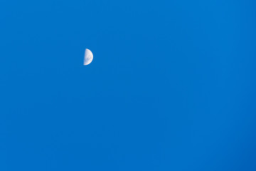 Blue daytime sky with half moon. Earth satellite on a blue.