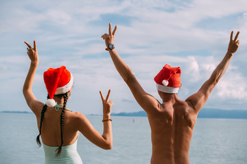 Young couple rejoice in Christmas caps on the ocean on a tropical island.