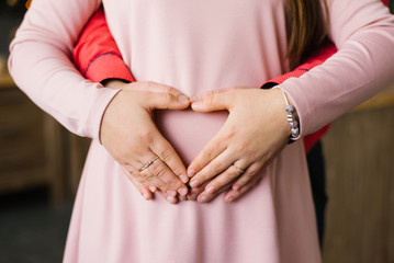 The palms of a pregnant woman and her husband on her stomach in the form of a heart