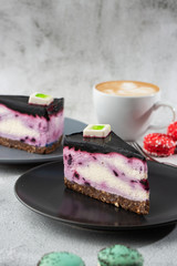 Cheesecake with blueberry with cup of coffee on white table. Closeup view. Tasty breakfast. Piece of cake on black plate, white cup on white marble background. Vertical photo.