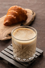 Cup of coffee cappuccino in transparent glass with french fresh croissant, old rusty background