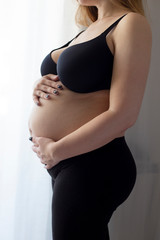 Portrait of young pregnant attractive woman, standing by the window