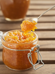 Tasty, homemade orange jam in a glass jar on a vintage wooden background. Dessert spoon with jam over the jar. Healthy citrus dessert. Close-up