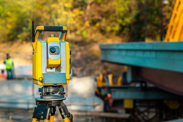 Surveyor engineer with equipment (theodolite or total positioning station) on the construction site of the road, building or bridge with construction machinery background