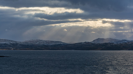 Mountains by a fjord with some snow and sunlight showing through clouds in northern Norway