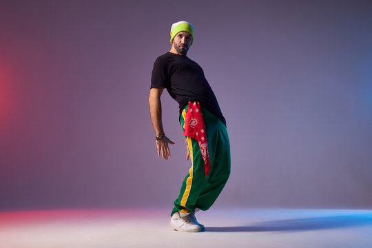 Young active man dressed in sportswear, performing hip hop style dance, training in dance studio, bending back, expressing emotions, looking at camera with brutal expression, street dance