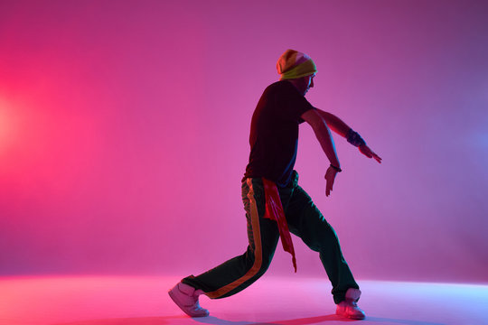 Handsome young professional hip hop dancer performing on stage of dance school, preparing for concert, exercising new movie, training hard in smoky dark studio