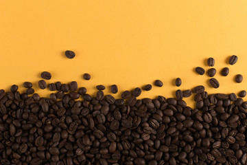 Coffee beans are scattered on a yellow paper background close-up, concept, commercial copy space.