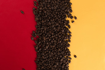 Coffee beans are scattered on a red and yellow paper background close-up, concept, commercial copy space.