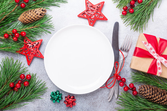 Christmas table place setting with empty white plate, gift box, cutlery with festive decorations star bow ball on stone background. Christmas and New Year holiday concept - Image