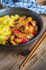 Saffron rice with pieces of chicken and vegetables on wooden table.