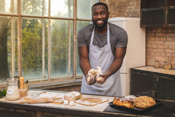Baking process. Cheerful dark skinned African American male wears apron, kneads dough with great enthusiasm, being content to recieve praise from chef for endeavour and hard work in restaurant.