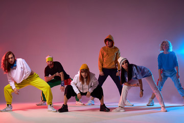 Young pretty group of professional dancers exercising modern dance movies, preparing for big concert, training in dance studio, performing on pink coloured background