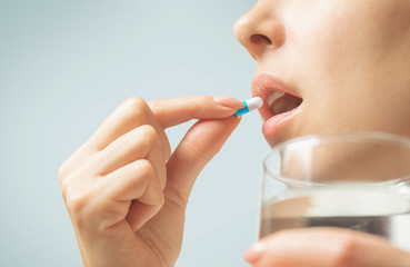 Woman taking a medication capsule or vitamin with glass of water. - 302059800