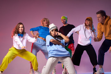 Attractive serious street style dancer performing at concert, surrounded by active hip hoppers, standing on knees, looking straight , keeping hand on cheek, expressing thoughtfulness