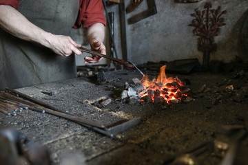 blacksmith holds red-hot metal by tongs in the forge furnace