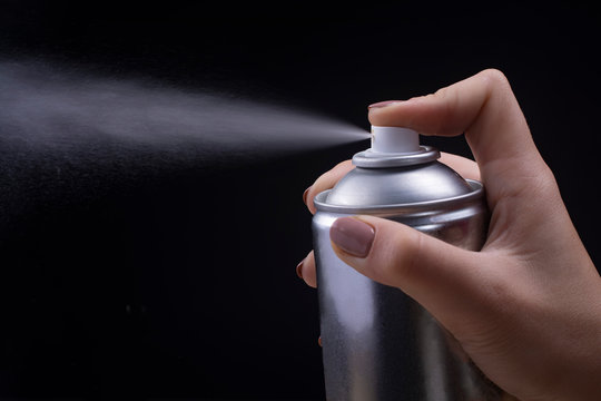 Female hand holds an aerosol can on a black background.