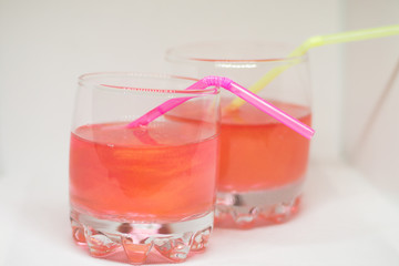 Two refreshing pink drinks with glitter and a straw for cocktails isolated on a white background