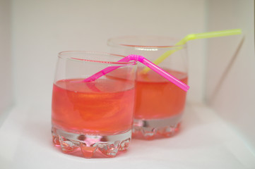 Two refreshing pink drinks with glitter and a straw for cocktails isolated on a white background