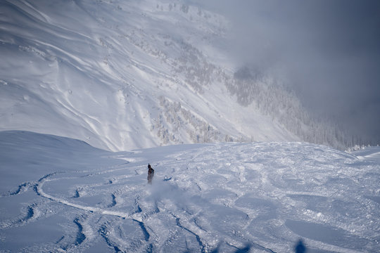 Image of a snowy surface covered by ski marks and man skiing down
