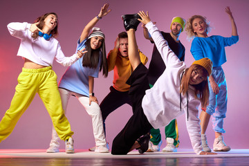Young group of teenagers spending birthday party in dance studio, practicing hip hop movies, jumping cheerfully, breakdancing on floor, indoor shot, modern style dancers concept