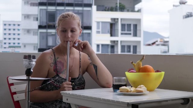 girl smokes a hookah on the balcony next to fruit and drink, overlooking the city