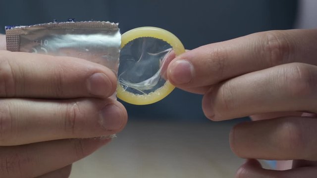 Male hands take out a condom from the packaging. Contraception and protected sex concept