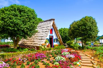 Fotobehang Amazing traditional houses in Santana, Madeira, Portugal. Wooden, triangular houses represent a part of Portuguese heritage. Front garden with beautiful colorful flowers. Tourist landmark © ppohudka