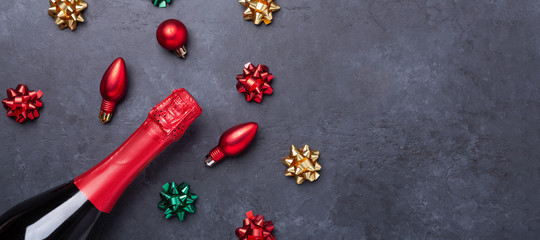 Christmas composition with champagne and red, green, gold gifts and bows on dark stone background. Horizontal banner. Christmas and New Year holiday concept - Image