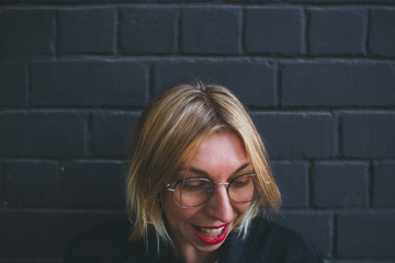 Portrait of a blonde in glasses on a brick wall background.
