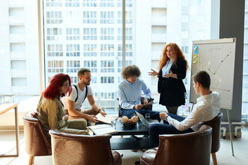 Female employee trying to present a report on company efficiency to her colleagues, but they are not paying attention. A group of 5 people at the office space demonstrating unhealthy work environment