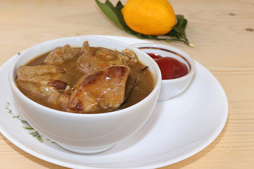 Closeup of meat goulash in a light cup on a wooden table with lemon, rustic simple style, selective focus. Roasted meat with sauce,