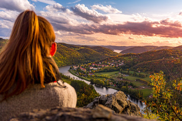 Beautiful girl enjoying life and watching the river, mountains and hills during sunset on the...