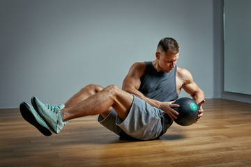 Strong man doing exercise with med ball. Photo of man perfect physique on grey background. Strength...