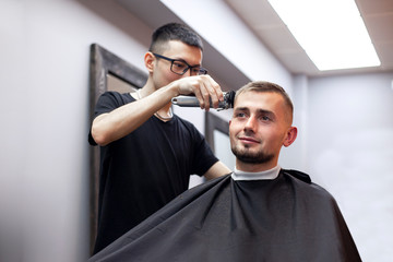 Kazakh barber gives the client a short haircut with a trimmer, a man has a haircut in a barbershop, guy does a hairstyle in a hairdresser