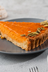 Portion of delicious bright orange pumpkin open pie on gray plate, decorated with pumpkin seeds with dessert forks close-up, top view. Bright marble background. Copy space. Vertical. menu for cafe