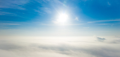 Aerial photo above the fog or white clouds with shining sun. Beautiful sunrise cloudy sky from aerial view. Above clouds from airplane window or drone.