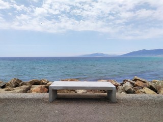 Stone bench on the coast. Dam to the island of Palomas in Spain. View of the Mediterranean Sea and...
