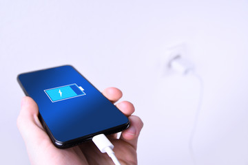 A human ,man hand puts charge the battery mobile smart phone, cellphone ,mobile on the white background with a socket in the frame.