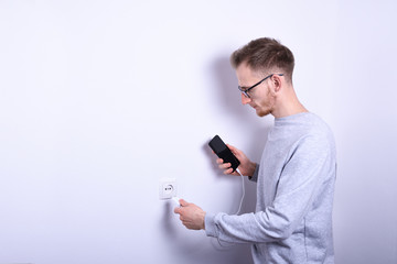 A human ,man hand puts charge the battery mobile smart phone, cellphone ,mobile on the white background with a socket in the frame.
