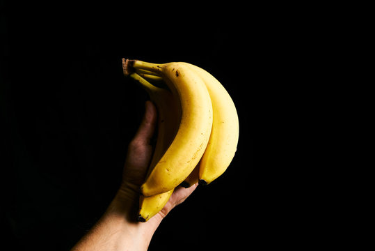 Fresh yellow babanas in the man hand isolated on black background with copyspase for cards and design for healthy life.