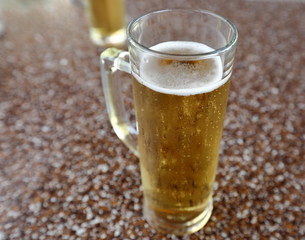 glass of beer on table, in background another glass in soft focus