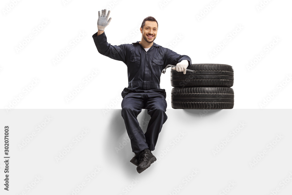 Wall mural Auto mechanic sitting on a panel with tires and a wrench and waving at the camera