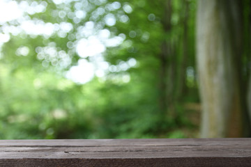 Plakat Image of grey wooden table in front of abstract blurred background of trees on a green meadow