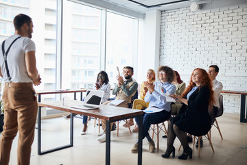 Ambitious young caucasian coach leader give presentation to co-workers sitting listening to him in modern office