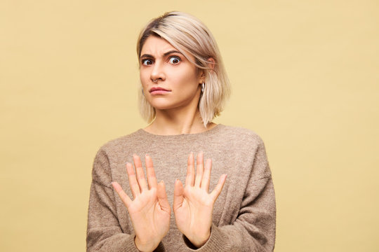 Portrait of outraged furious young European blonde woman expressing indignation, reaching out hands, making No or Stop gesture, saying Stay away from me while having fight with her boyfriend