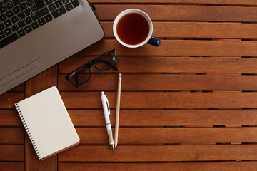 Office table with laptop computer, cup glasses on wooden background