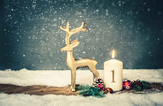 burning candle from 1st advent in front of vintage background and decorative christmas background in snow
