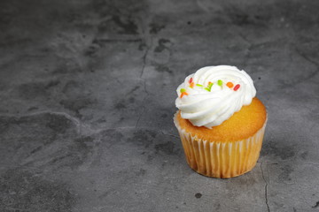 Sweet Cupcakes with cream frosting and rainbow sprinkles on grey background.