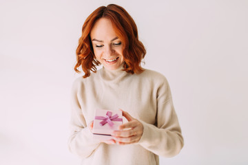 Young birthday girl smiles, holding a pastel coloured gift box with pink ribbon. Happy woman, peeking inside a gift box.